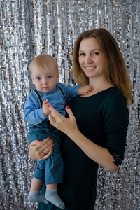 一位年轻的母亲和她的儿子在银色背景的亮片上的美丽肖像。