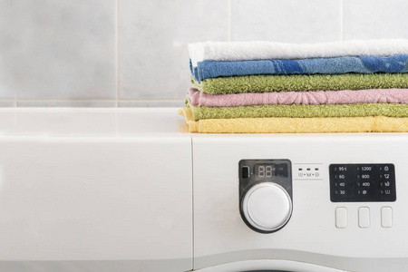 一堆五颜六色的毛巾躺在洗衣机上的洗衣房里