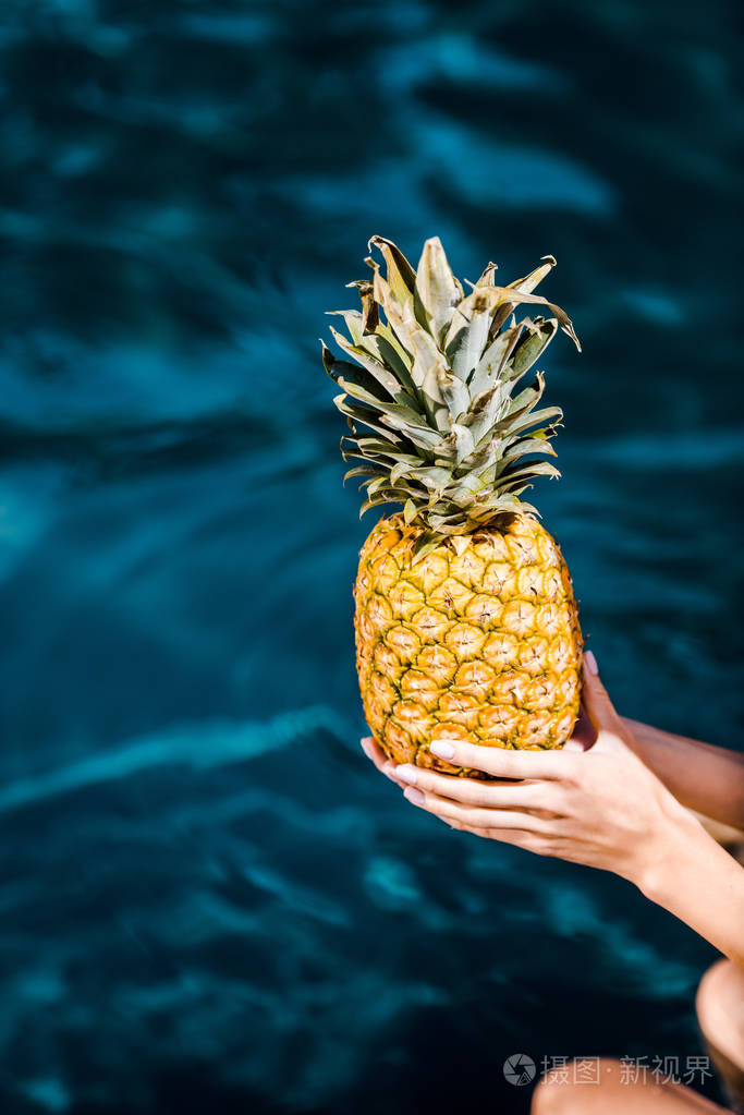 在游泳池附近摆姿势拿着新鲜菠萝的女孩的局部景色