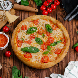 带西红柿奶酪和新鲜罗勒叶的比萨饼的顶部，放在木桌上