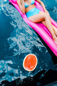 躺在带西瓜的游泳池里的粉红色充气床垫上的女孩