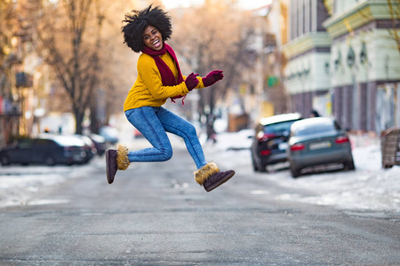 穿着围巾和毛衣的年轻黑人女人在街中央跳跃。