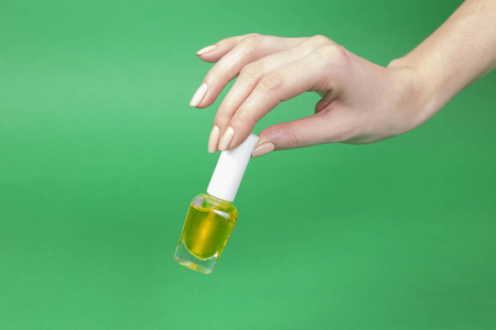 s hand holding bottle with yellow nail polish of green backgroun