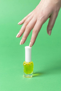 s hand holding bottle with yellow nail polish of green backgroun