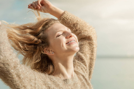 快乐微笑的金发女人肖像。 快乐的女性积极地走在户外，穿着有风的毛衣，在阳光下披散着头发