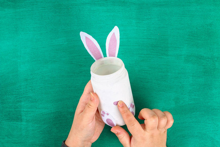 迪伊复活节花瓶兔子从玻璃瓶感觉到绿色的背景。 春天复活节的礼物创意装饰。 手工制作。 一步一步。 手工艺的过程。 上面的风景。 