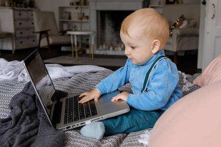 一个小男孩坐在一张大床上，好奇地看着笔记本电脑。