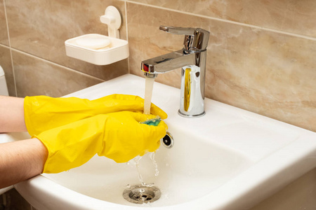 s hands in yellow protective rubber gloves with green sponge und