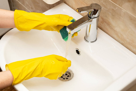 s hands in yellow protective rubber gloves with green sponge und