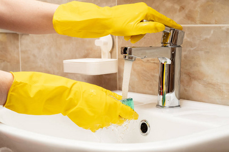 s hands in yellow protective rubber gloves with green sponge und