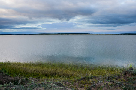 傍晚在灰色多云的天空下平静的湖。
