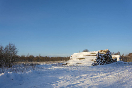 在一个晴朗的冬天，道路边缘有一大堆雪覆盖的原木。