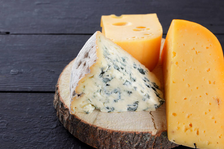 不同类型的奶酪在黑板上.瑞士奶酪和dorblu在黑暗的背景下.