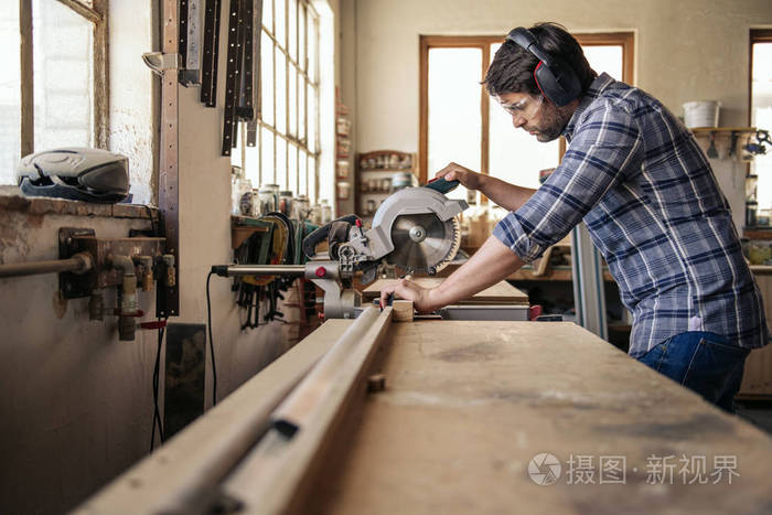 熟练的木工在木工工作室独自工作时 穿着安全用具用锯子锯一块木头照片 正版商用图片17lddh 摄图新视界 熟练的木工在木工工作室独自工作时 穿着安全用具用锯子锯一块木头照片 正版商用图片17lddh 摄图新视界