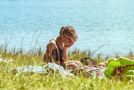 那个女孩在海滩上很伤心。阳光明媚的一天，一个穿着泳衣的女孩孤独地坐在河边的草地上的海滩上。
