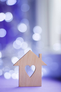 房子的木制图标，洞的形式，心脏在近窗户在白天，波克灯在模糊的紫色背景。带有复制空间的浪漫卡片。甜蜜的家的概念。