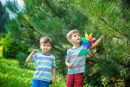 两个快乐的孩子在花园里玩风车手轮。 可爱的兄弟姐妹是最好的朋友。 可爱的男孩微笑春天或夏天公园。 户外休闲友谊家庭概念。