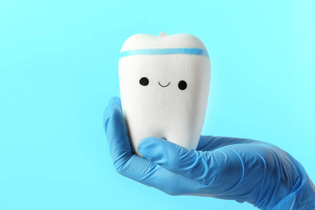 牙科医生在彩色背景上用可爱的脸持有牙齿模型