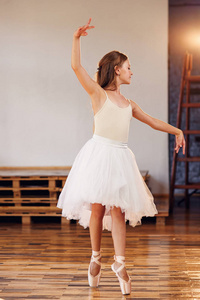年轻的芭蕾舞演员穿着白色的芭蕾舞裙练习舞蹈动作。 舞蹈学校穿芭蕾舞裙的年轻女孩。
