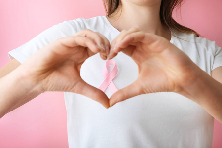 女人用粉红色的丝带做心脏，用她的手特写。 乳腺癌意识概念