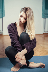 年轻的金发女人坐在瑜伽垫上。 色调的图像。