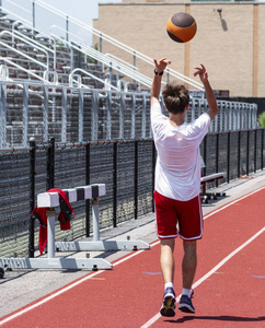 一名高中运动员正在一条红色的赛道上，在漂白剂中，后投掷一个药球，以获得力量速度和敏捷性的练习。
