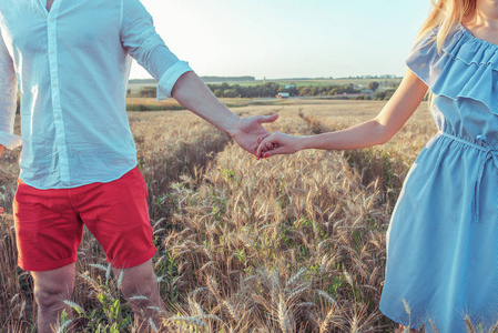 一个男人和一个女孩在夏天去麦田, 牵着对方的手。在农村的特写夏天。婚姻中幸福关系和强烈爱情的概念