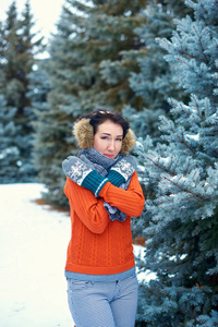 女人在冬天的森林里摆姿势，美丽的风景和雪杉树。 穿着红色毛衣和耳罩