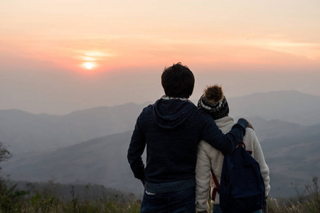 爱的一对情侣在日落时拥抱在山上,面对美丽的风景.照片