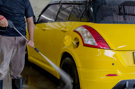 工人用高压垫圈在黄色汽车上清洗汽车。