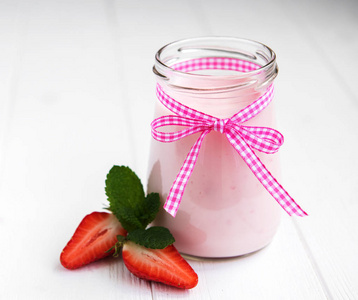 白色木桌上放着草莓酸奶的罐子
