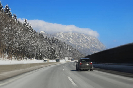 汽车在空旷的冬季公路上行驶, 背景上覆盖着美丽的山, 覆盖着雪。冬季旅行和度假