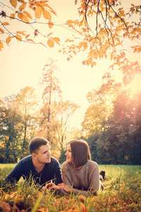 一对年轻漂亮的夫妇躺在秋天公园的草地上