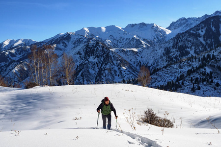 山里的旅行者穿着雪鞋走路。 一个年轻人走在白雪中间。 他手里拿着徒步旅行的电线杆。 冬季山地旅游。 哈萨克斯坦