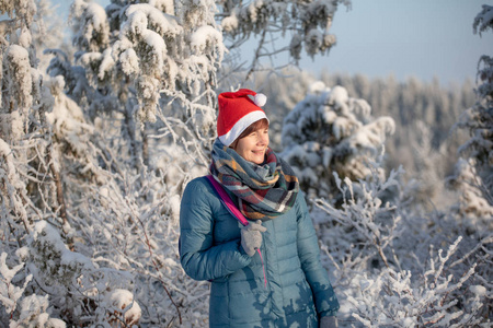 一个戴着红色圣诞帽的年轻女孩站在河岸上。 霜雪的冬日