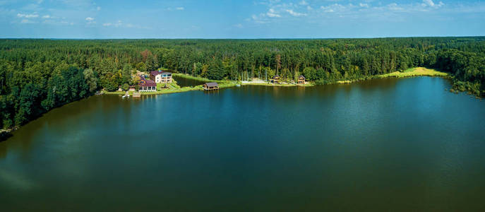 湖边的木屋，水清澈。池塘映着茂密的绿色森林和白色皮肤的天空。湖上舒适的小私人住宅。美丽的风景。