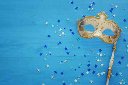 嘉年华派对庆祝概念与优雅的黄金面具上的棍子蓝色木制背景和明星。 顶部视图