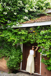 一个浪漫的女人站在老门旁边，在一丛盛开的花丛下