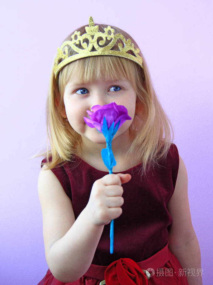 可爱的女孩头上戴着皇冠,闻着粉红色的玫瑰. 穿着漂亮衣服微笑的孩 
