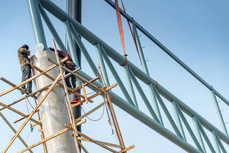 桁架结构男建筑工人站在木脚手架上,在施工现场的混凝土柱上焊接钢