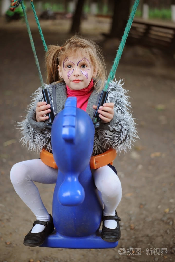 一个女孩在公园里骑秋千. 女孩的脸上画着粉红色的蝴蝶.