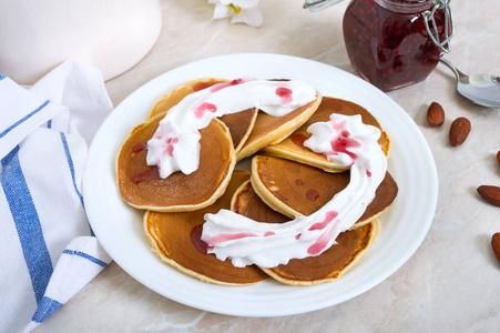 厨房桌子上的白色盘子上有覆盆子果酱和鲜奶油的美味煎饼。 经典的美国自制早餐。