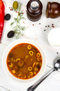 传统的俄罗斯汤索扬卡用肉香肠盐渍黄瓜和橄榄煮熟。木桌上的白色砂锅