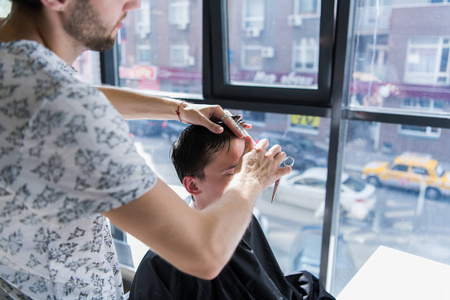 一个专业的发型师, 手里拿着梳子和剪刀, 在发廊里造型男人的湿黑短发