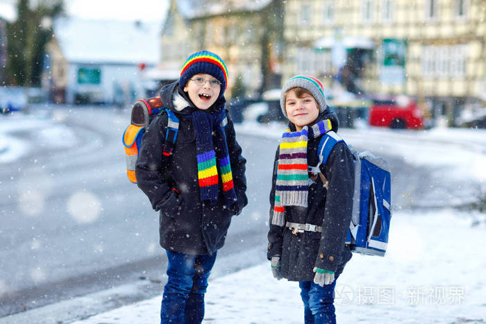 两个小学生在下雪的时候步行去学校.快乐的孩子玩第一次雪.