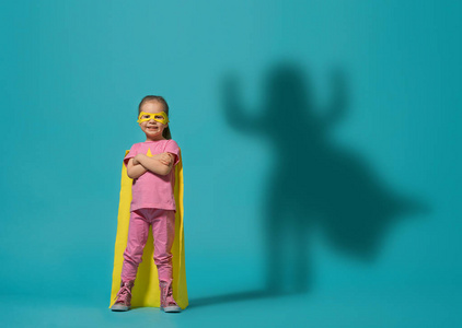 玩超级英雄的小孩子。 亮蓝墙背景上的孩子。 女孩权力概念。 黄色粉红色和绿松石颜色。