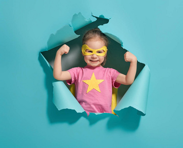 玩超级英雄的小孩子。 亮蓝墙背景上的孩子。 女孩权力概念。 黄色粉红色和绿松石颜色。
