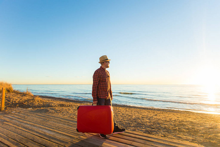 旅行旅行暑假和假期的概念一个穿红色箱子的人站在海滩上看日落