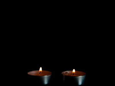 两支点燃的蜡烛，带着橙色的火焰，孤立在黑色的背景上