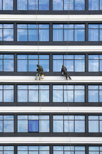 两名工人在高层建筑清洁窗户服务。 工人们清洗现代摩天大楼的正面窗户。 工人们修理摩天大楼的正面。